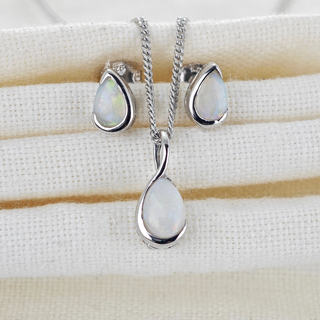 Natural opal pendant and stud set in infinity loop of sterling silver on a fabric jewellery rest